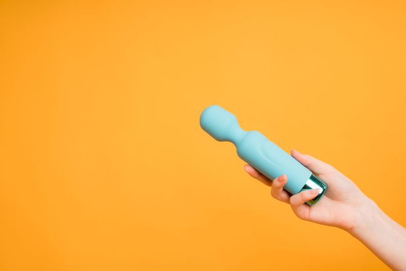 a yellow background reveals a hand holding a blue vibration device.