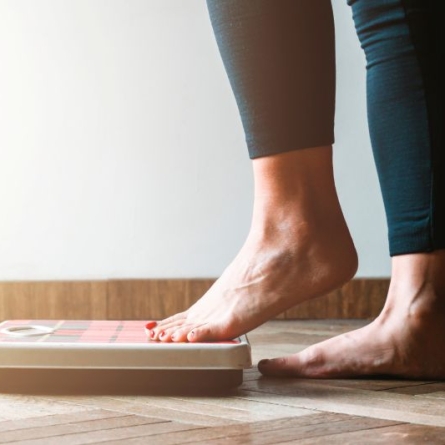 Foot with red painted toenails and legging-covered lower leg gently stepping on home scale