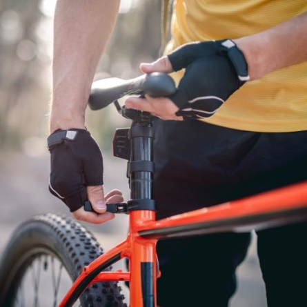 Cyclist with yellow shirt and black gloves adjusting black bicycle seat on orange frame