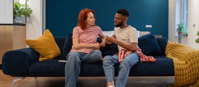 Red-haired woman and bearded man sitting on dark blue couch having a serious conversation