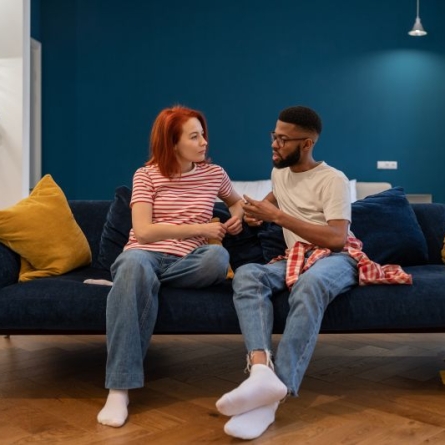 Red-haired woman and bearded man sitting on dark blue couch having a serious conversation
