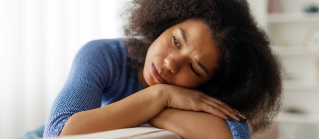 Woman resting head on crossed arms over back of couch looking distressed