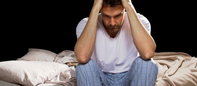 Man sitting on bed in pajamas, distressed with head in hands