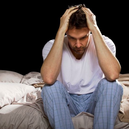 Man sitting on bed in pajamas, distressed with head in hands