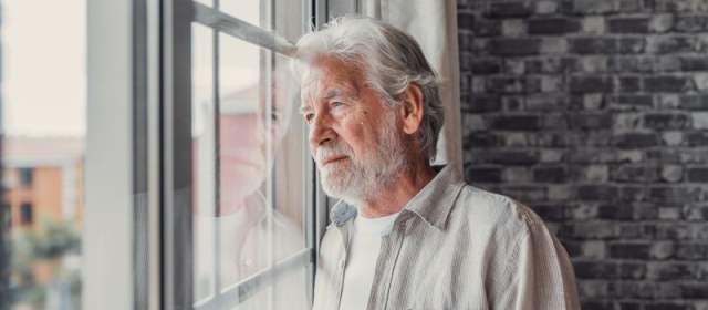 Graying man staring out widow in deep thought