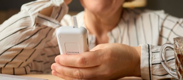 Older woman holding blood sugar monitor, insulin injection on table in front