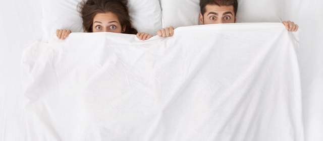 Man and woman surprised under white comforter