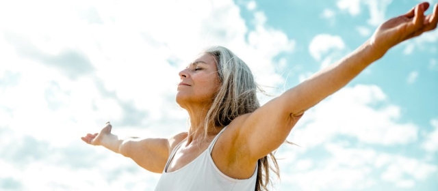 Woman with arms outstretched breathing in outdoor air