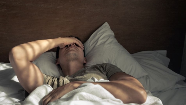 Man lying in bed, hand over head in distress.