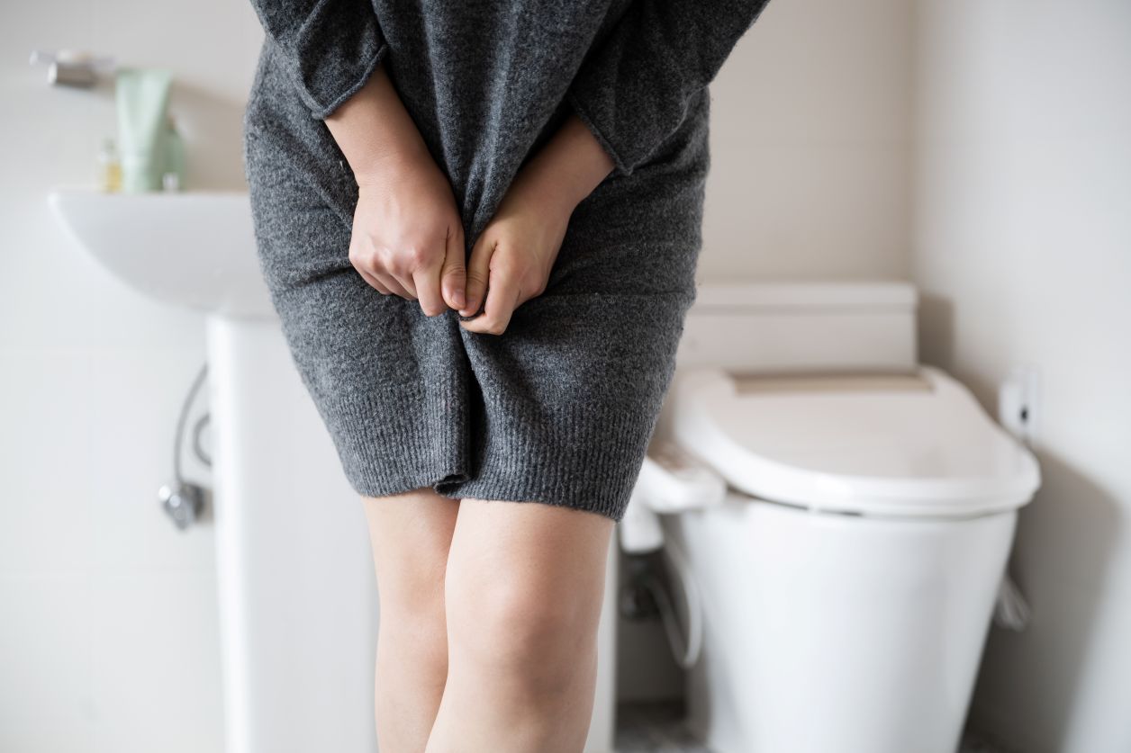 woman in bathroom holding sweater dress over bladder, legs crossed