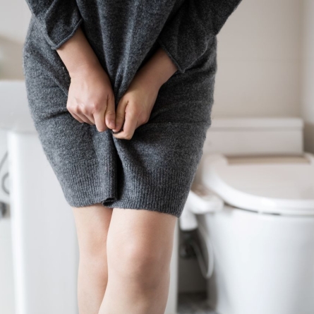 woman in bathroom holding sweater dress over bladder, legs crossed