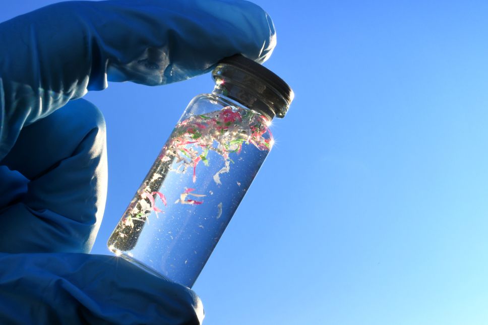 gloved fingers holding vial of microplastic-filled water