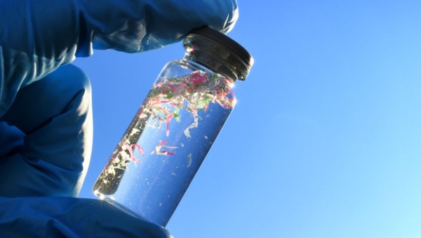 gloved fingers holding vial of microplastic-filled water