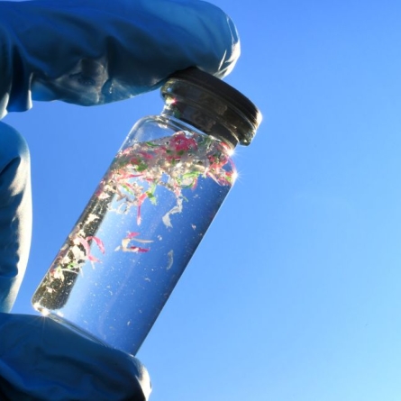 gloved fingers holding vial of microplastic-filled water
