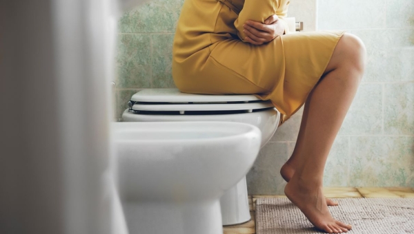 woman in yellow dress on toilet holding stomach