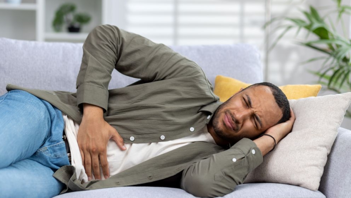 man laying on side on a couch holding stomach and head in pain