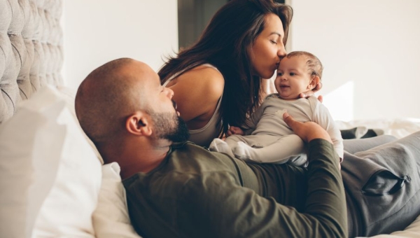 dad laying down holding baby, mom leans over and kisses baby on forehead