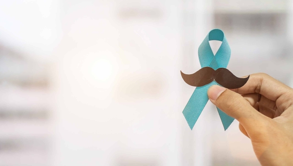 A hand holding a blue awareness ribbon and moustache for Movember