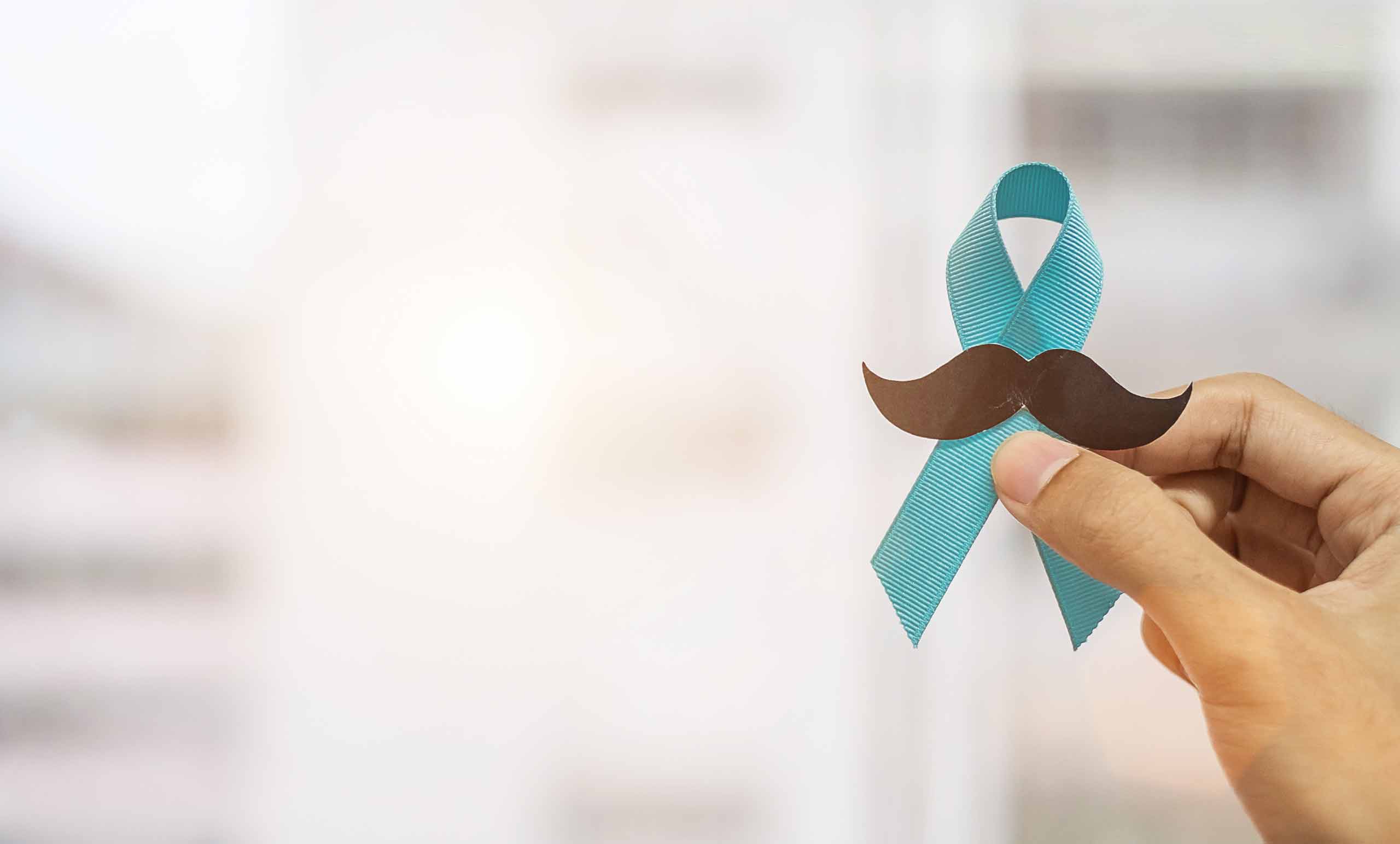 A hand holding a blue awareness ribbon and moustache for Movember